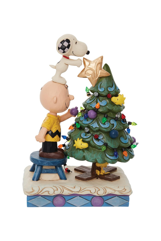 Ornament depicting Charlie Brown standing on a stool, decorating a Christmas tree. Snoopy is on his head putting the star on top. 