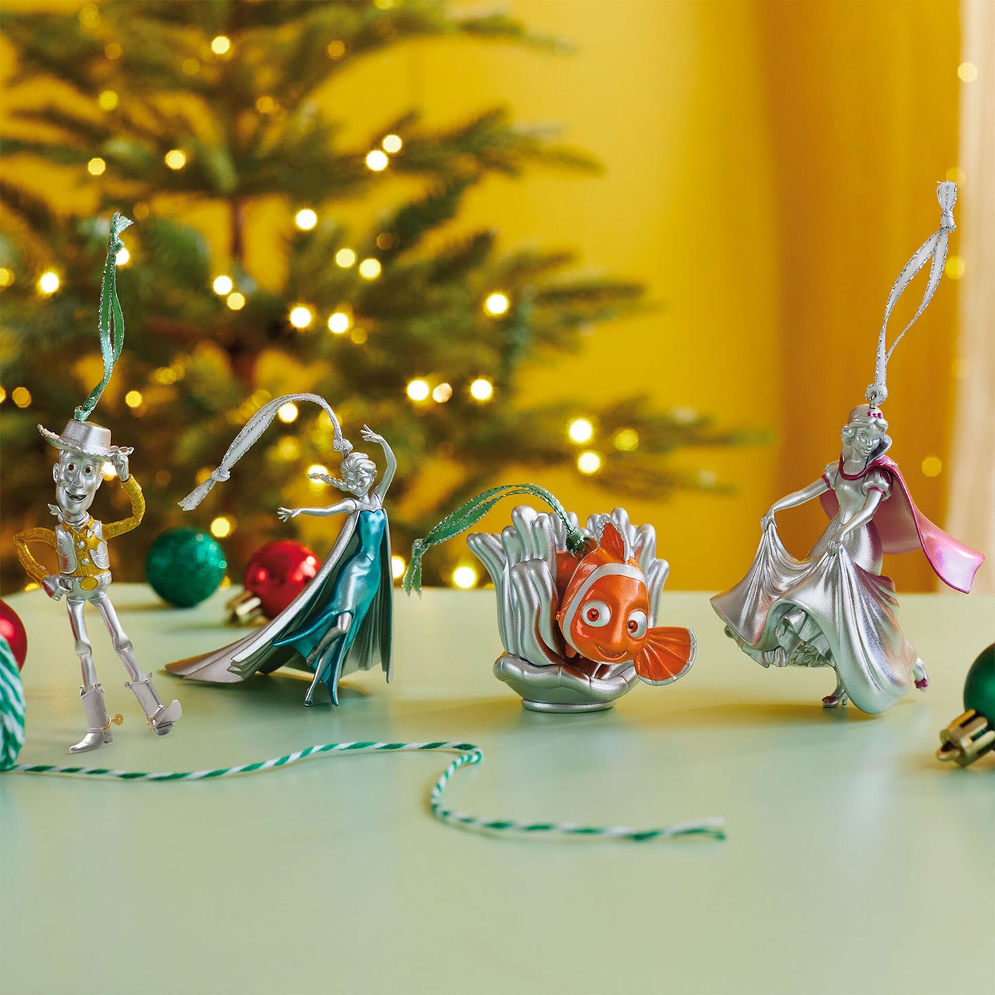 Four metallic silver Disney character Christmas ornaments. The characters from left to right are Woody, Elsa, Nemo, and Snow White.