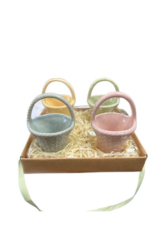 Four glass Easter baskets (blue, pink, yellow, and green) sitting on a bed of straw in a shallow box.
