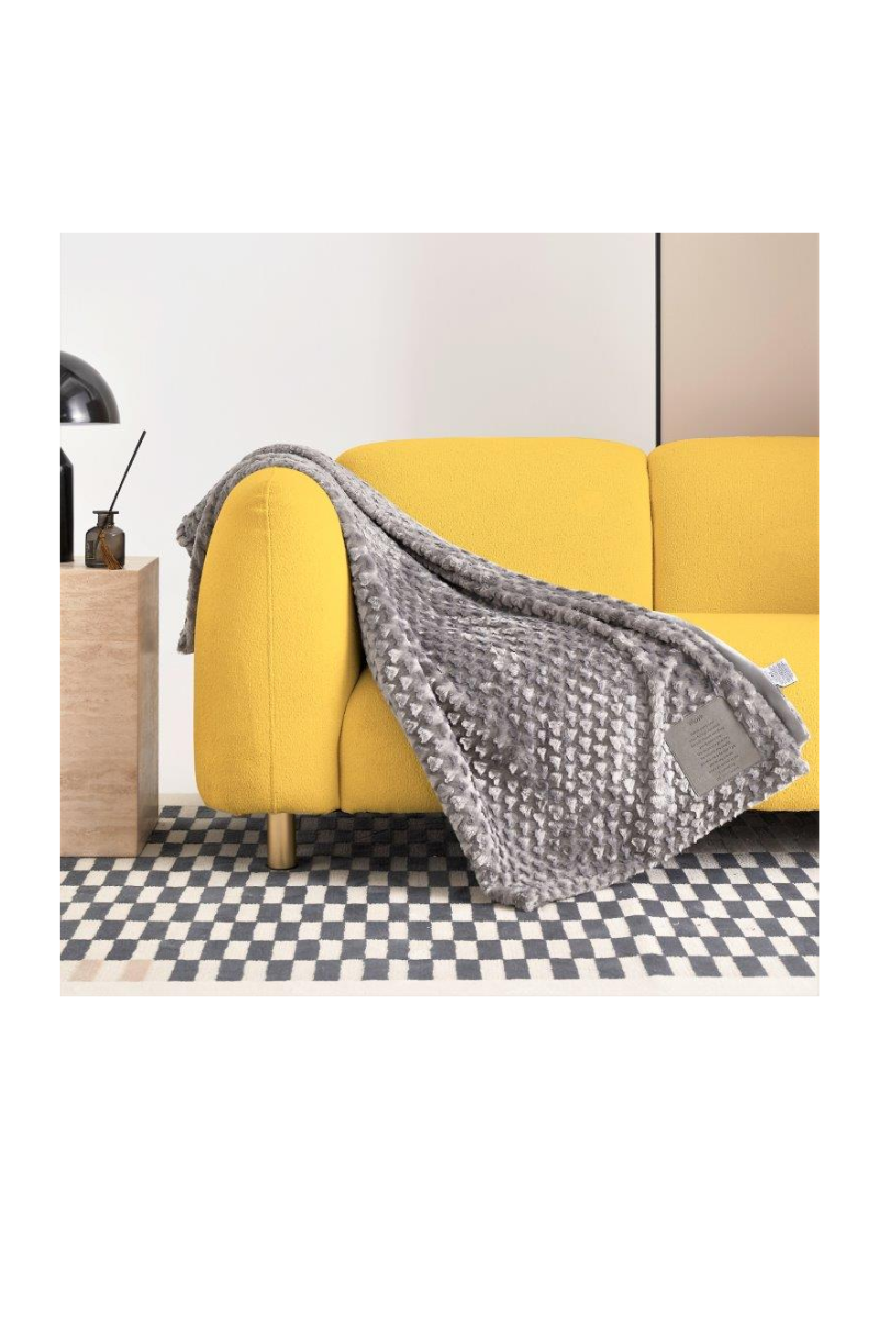 A grey blanket, with a patch that can be personalized, draped over the arm of a yellow couch.