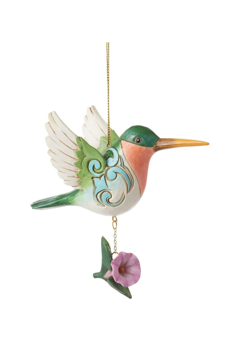 A green, white, and orange hummingbird ornament with blue carved embellishments and a purple flower hanging from its belly.