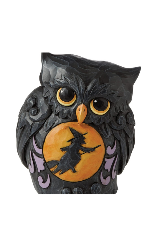 A carved black owl figurine with an orange moon carved on its belly. The silhouette of a witch flying on a broom is carved in front of the moon. 