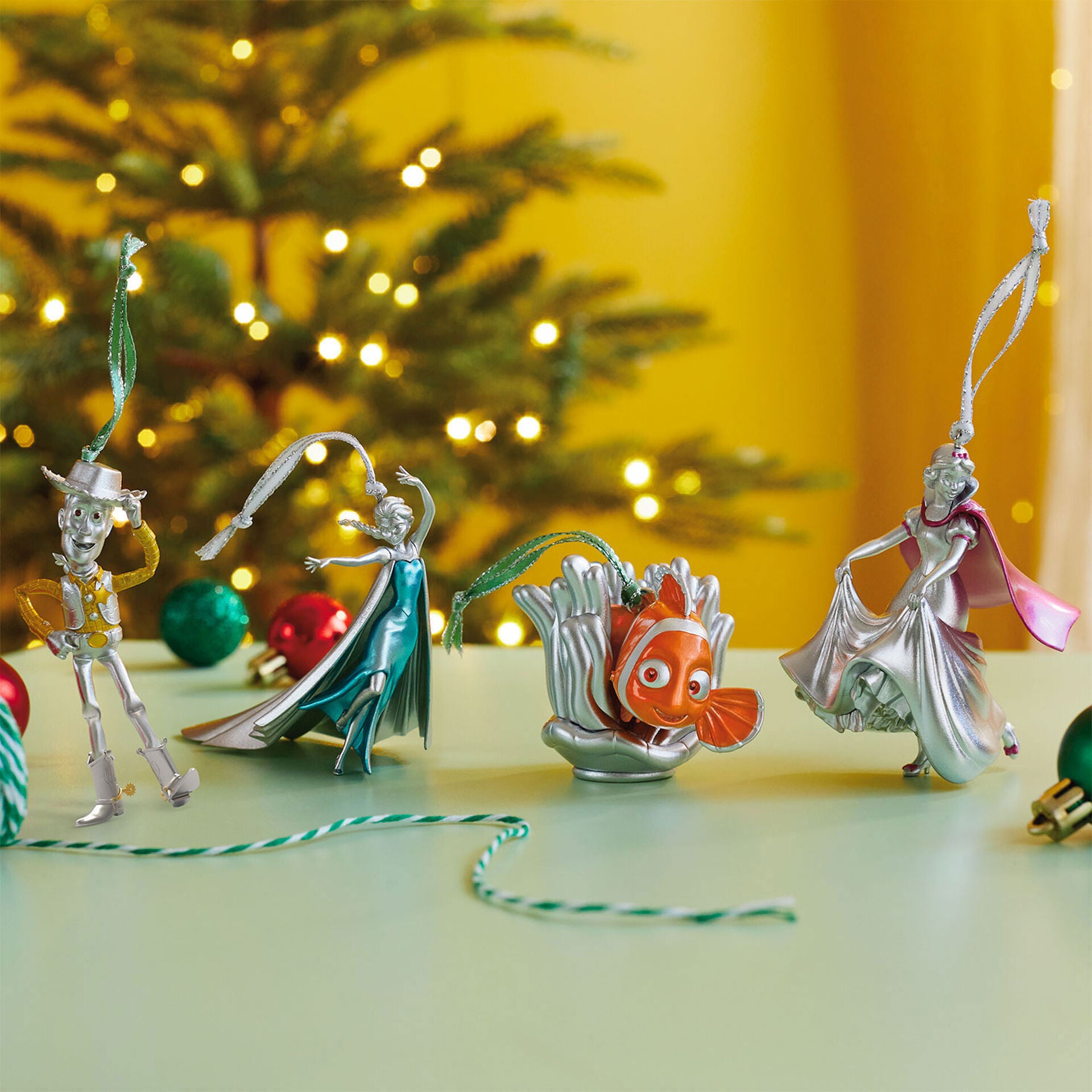 Four metallic silver Disney character Christmas ornaments. The characters from left to right are Woody, Elsa, Nemo, and Snow White.