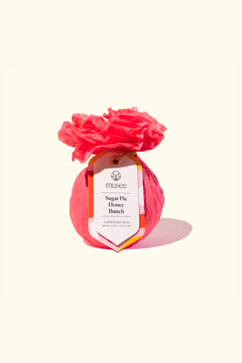 Musee bath bomb wrapped in bright pink tissue paper. 