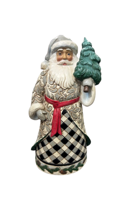 A rustic Santa figure with black and white checkered robe holding a small Christmas tree.