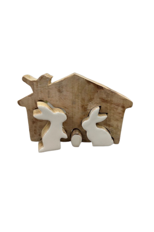 A wooden silhouette of a house with a bird perched on the roof. Two white bunnies with a white egg between them are inlaid in the wood.