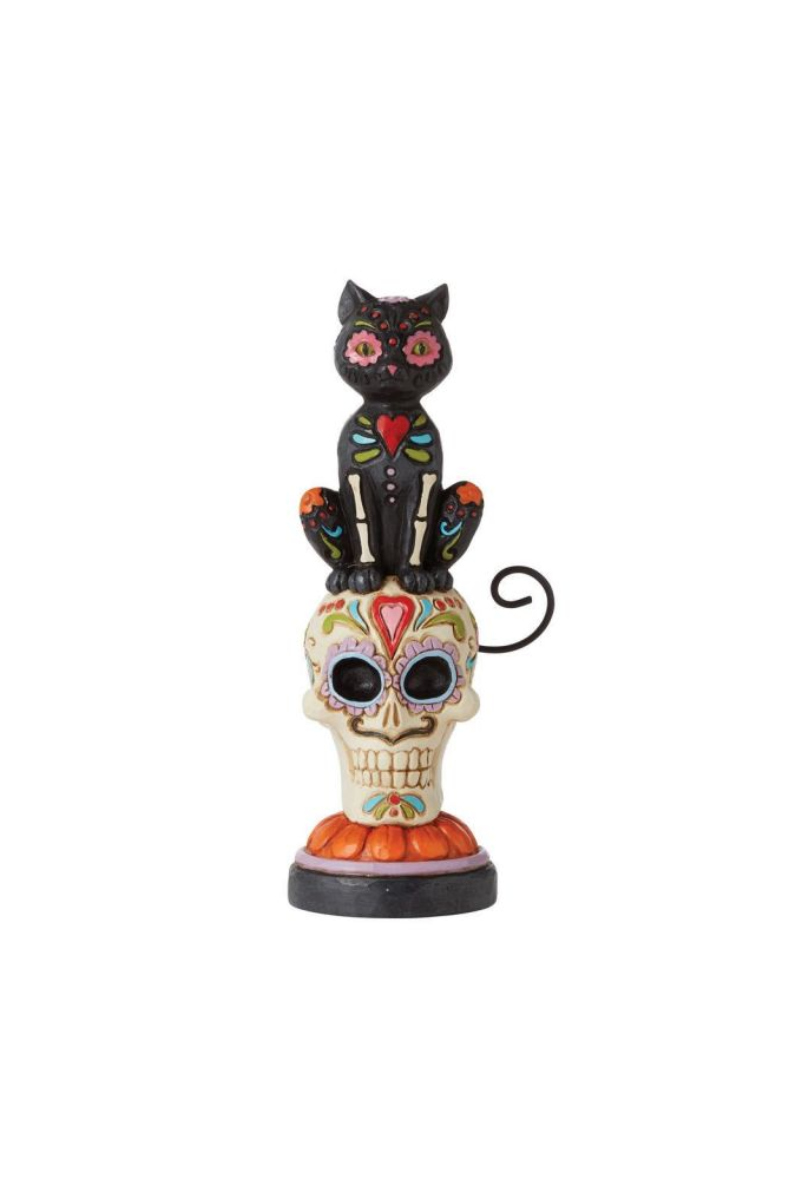 A black cat sitting on stop of a Day of the Dead skull.