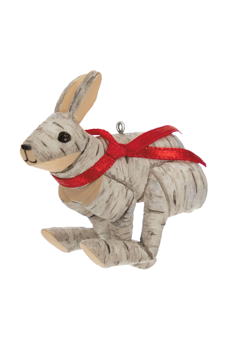 A Christmas ornament of a rabbit made out of pieces of birch wood with a red ribbon tied around its neck. 