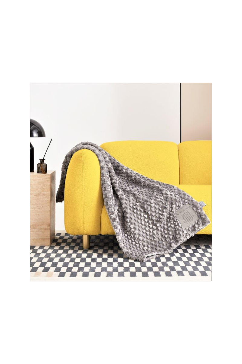 A grey blanket, with a patch that can be personalized, draped over the arm of a yellow couch. 