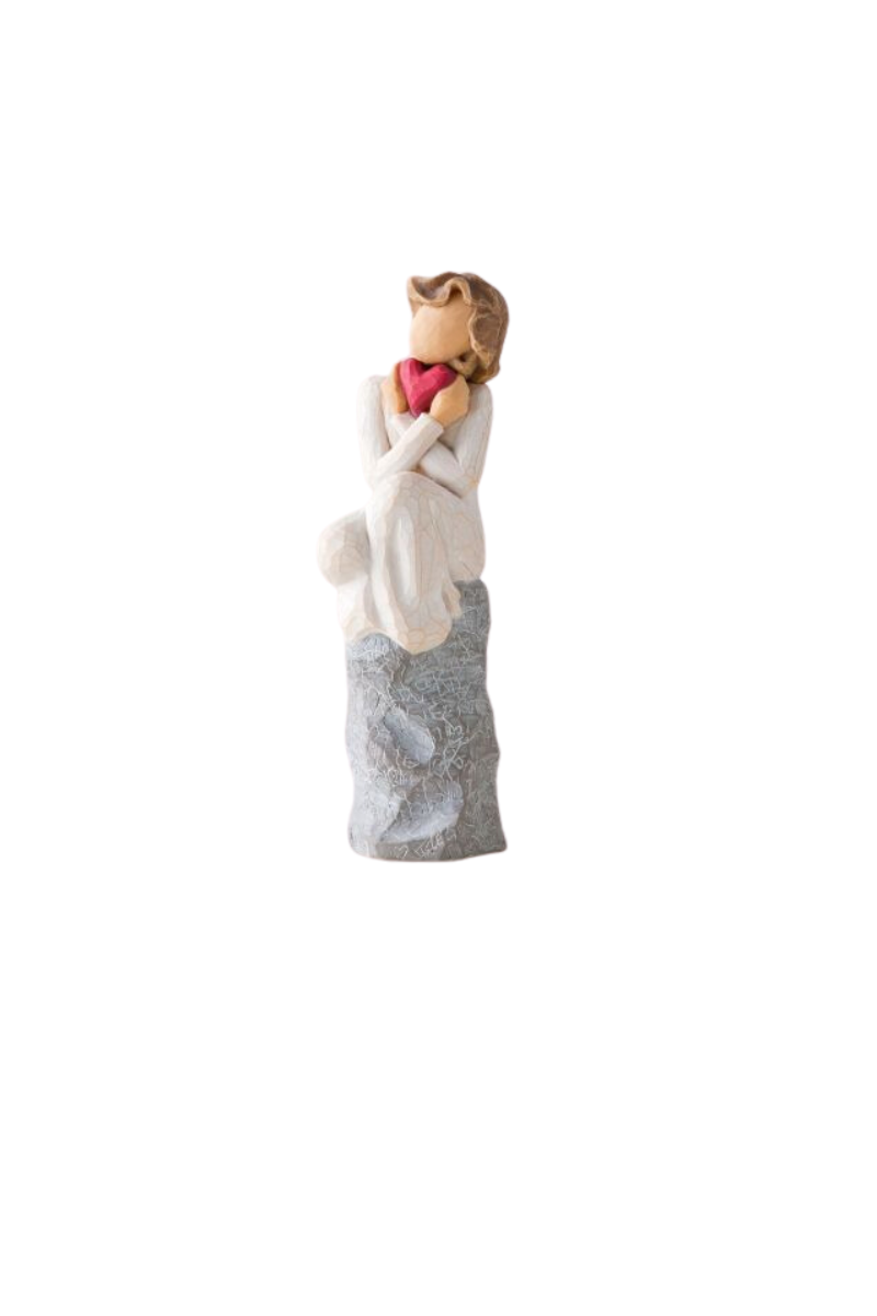 A Willowtree figure of a girl in white with brown hair sitting on a stone, holding a red heart.