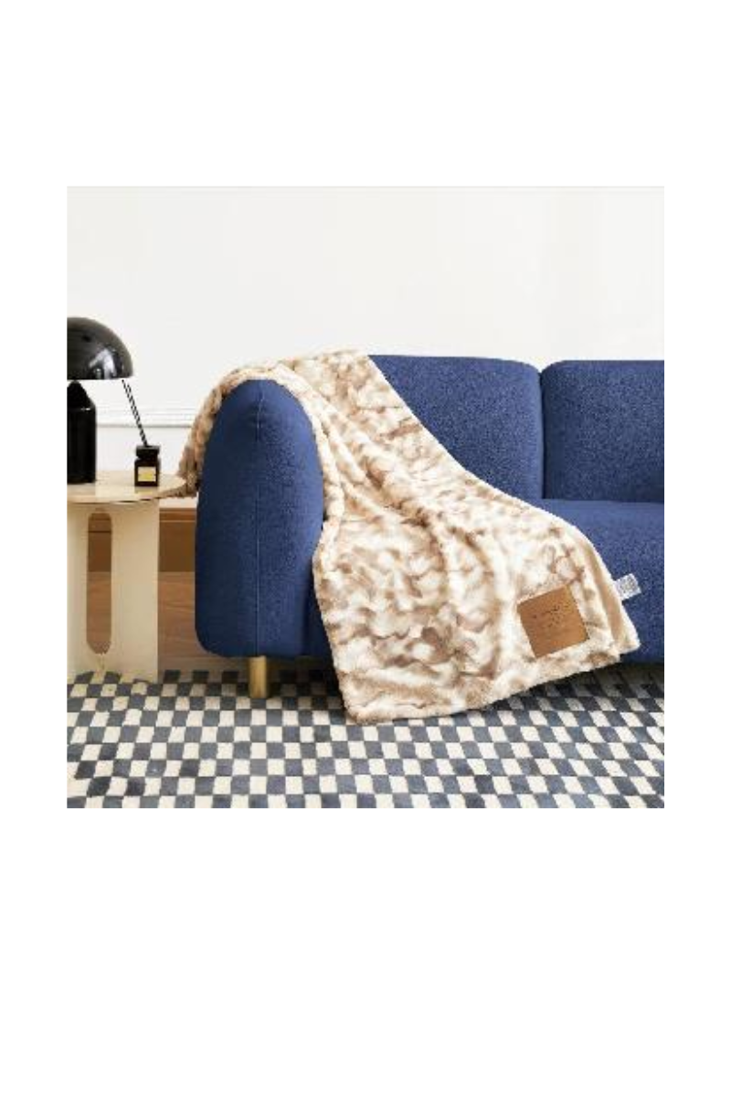 A tan and white blanket draped over a navy blue couch. 