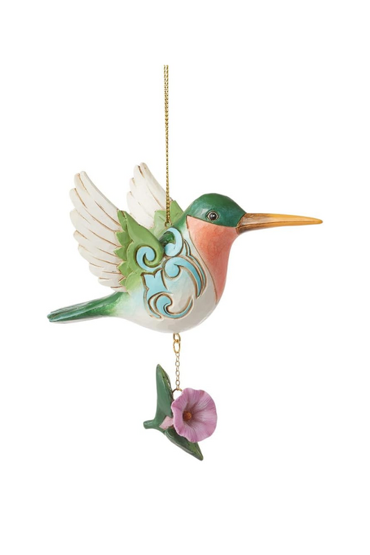 A green, white, and orange hummingbird ornament with blue carved embellishments and a purple flower hanging from its belly. 
