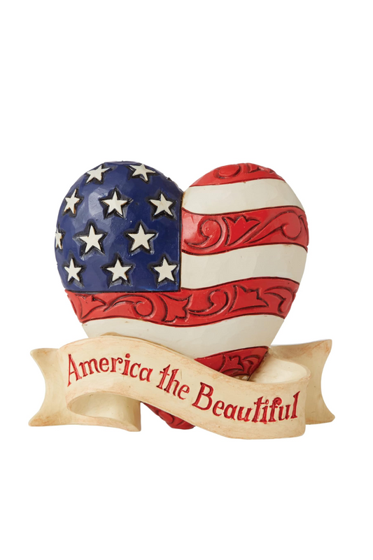 A figurine of the American flag in the shape of a heart with carved embellishments and a white ribbon across the front that reads America the Beautiful.