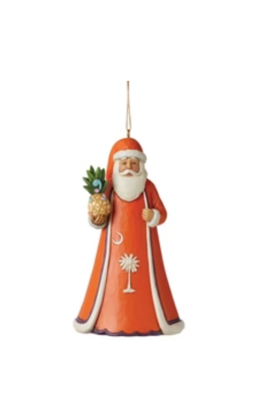 A Santa ornament with the crescent moon and palm tree of the South Carolina state flag on the front of his robe. He is holding a pineapple.