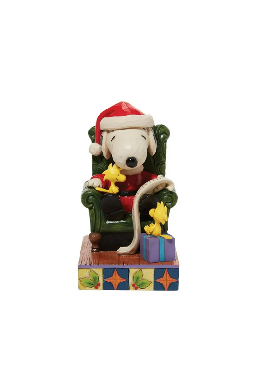 Ornament depicting Snoopy wearing a Santa outfit, sitting in a green chair holding a list. 